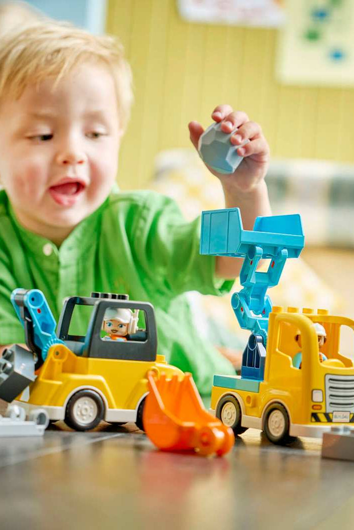 A close-up view of a child's hands using the tipping bucket loader to dump a boulder block into the DUPLO dump truck.