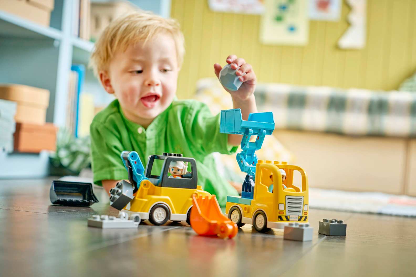 A close-up view of a child's hands using the tipping bucket loader to dump a boulder block into the DUPLO dump truck.